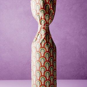 Pode incluir: Uma garrafa embrulhada em papel colorido com um padr&atilde;o de arcos-&iacute;ris e flores brancas. O papel est&aacute; amarrado com um el&aacute;stico.
