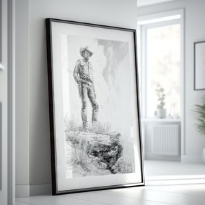 May include: A black and white drawing of a cowboy standing on a rocky cliff, framed in a black frame.