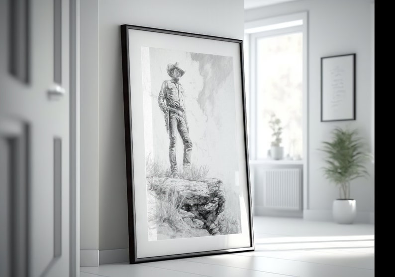 May include: A black and white drawing of a cowboy standing on a rocky cliff, framed in a black frame.