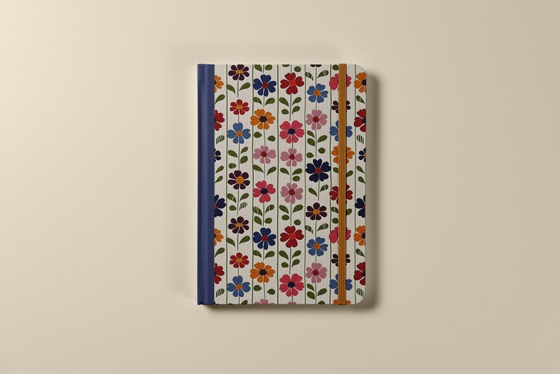 Pu&ograve; includere: Un quaderno bianco con un motivo floreale in tonalit&agrave; di rosa, rosso, blu, arancione e verde. Il quaderno ha una rilegatura blu e una chiusura elastica marrone.