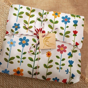 Pu&ograve; includere: Una borsa regalo bianca con un motivo floreale in tonalit&agrave; di blu, rosso, giallo e verde. La borsa &egrave; legata con uno spago bianco e rosso e ha un'etichetta marrone con il testo "Champagne & Cookies" in lettere dorate.