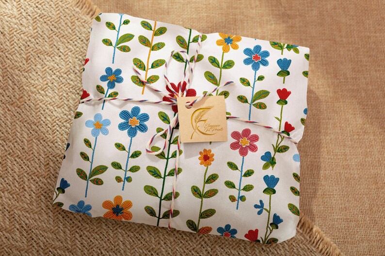 Pu&ograve; includere: Una borsa regalo bianca con un motivo floreale in tonalit&agrave; di blu, rosso, giallo e verde. La borsa &egrave; legata con uno spago bianco e rosso e ha un'etichetta marrone con il testo "Champagne & Cookies" in lettere dorate.
