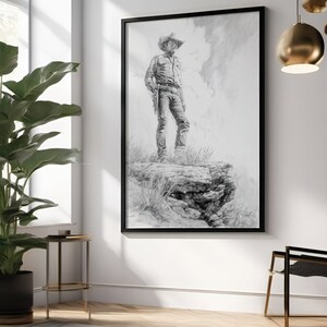 May include: Black and white drawing of a cowboy standing on a rock formation, framed in a black frame.