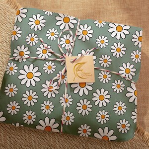 Pode incluir: Um presente embrulhado em papel verde com um padr&atilde;o de margaridas brancas. O papel &eacute; amarrado com barbante e uma etiqueta marrom que diz "Happy Mail" em letras douradas.
