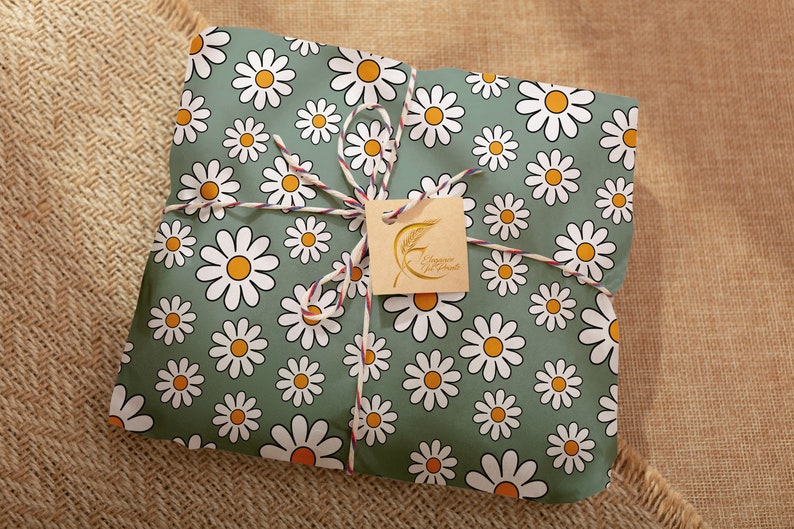 Pode incluir: Um presente embrulhado em papel verde com um padr&atilde;o de margaridas brancas. O papel &eacute; amarrado com barbante e uma etiqueta marrom que diz "Happy Mail" em letras douradas.
