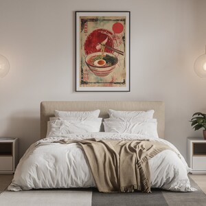 May include: A white bed with a tan blanket and two white pillows. A framed poster of a bowl of ramen with chopsticks hanging over the bowl is hanging on the wall above the bed. There are two nightstands with lamps on either side of the bed.
