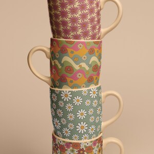 Pode incluir: Um conjunto de quatro canecas de cer&acirc;mica com diferentes padr&otilde;es florais. As canecas est&atilde;o empilhadas em ordem, de cima para baixo: flores cor-de-rosa, linhas onduladas com flores, margaritas brancas e flores laranja e rosa.
