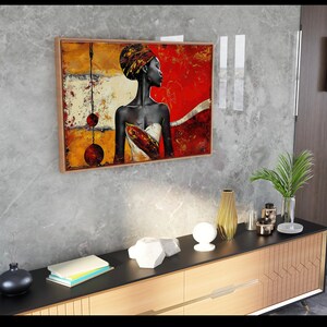 May include: A framed abstract painting of a woman with a colorful head wrap and a white dress. The painting is set against a textured gray wall and a wooden cabinet with a black top.