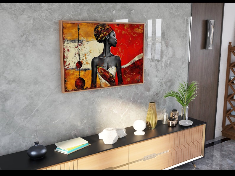 May include: A framed abstract painting of a woman with a colorful head wrap and a white dress. The painting is set against a textured gray wall and a wooden cabinet with a black top.