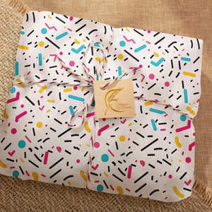 May include: A white gift bag with a colorful geometric pattern, tied with twine and a brown tag that says "Happy Holidays".