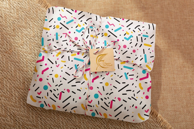 May include: A white gift bag with a colorful geometric pattern, tied with twine and a brown tag that says "Happy Holidays".