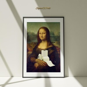 Può includere: Una stampa incorniciata della Gioconda che tiene un rotolo di carta igienica. La stampa è in una cornice nera e ha uno sfondo bianco.