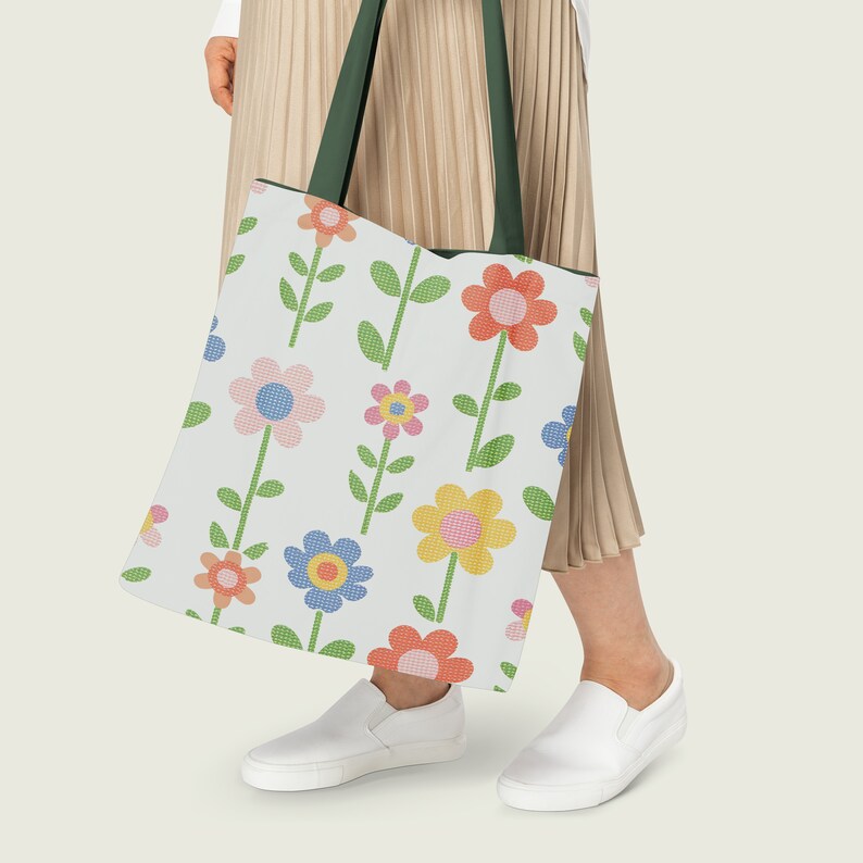Pu&ograve; includere: Una borsa tote bianca con un manico verde e un motivo floreale con fiori rosa, gialli, blu e arancioni. La borsa &egrave; tenuta da una persona che indossa una gonna beige.