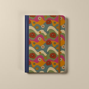 Pode incluir: Um caderno azul e marrom com um padr&atilde;o floral retr&ocirc;. O caderno tem um fecho de banda el&aacute;stica marrom e uma lombada azul.