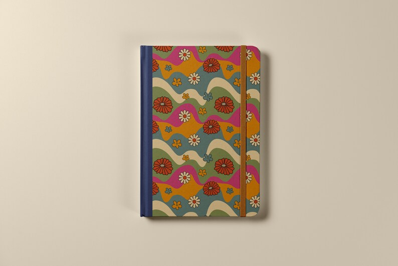 Pode incluir: Um caderno azul e marrom com um padr&atilde;o floral retr&ocirc;. O caderno tem um fecho de banda el&aacute;stica marrom e uma lombada azul.
