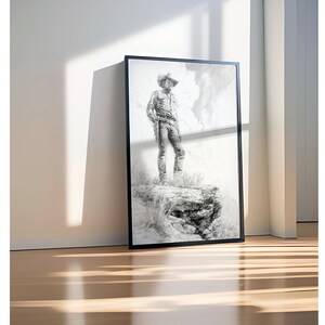 May include: A black and white drawing of a cowboy standing on a rock formation. The cowboy is wearing a hat and a long-sleeved shirt. The drawing is framed in a black frame.
