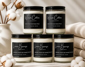 May include: Five clear glass jars filled with white wax and topped with black lids. Two jars are labeled Warm Cotton with Amber, Orris root, Ozone, Wood. Three jars are labeled Linen Breeze with Aldehydic, Peach, Lily, Jasmine, Wood Musk.