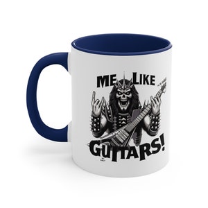 May include: White ceramic coffee mug with a navy blue rim. The mug features a black and white illustration of a skeleton playing a guitar with the text "ME LIKE GUITARS!"