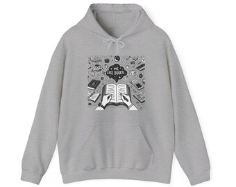 Puede incluir: Sudadera con capucha gris claro con un diseño gráfico en blanco y negro. El diseño muestra a una persona escribiendo en un libro, rodeada de libros, tazas de café y otros objetos. El texto "ME LIKE BOOKS!" está en una burbuja.
