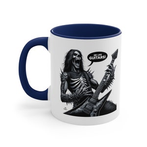 May include: White ceramic coffee mug with a navy blue rim. The mug features a black and white illustration of a skeleton playing a guitar with the text "ME LIKE GUITARS!" in a speech bubble.