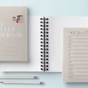 May include: Two beige spiral bound journals with a light brown cover. The journal on the left has the text "My PhD Bullet Journal" and space for a name, year, and project. The journal on the right has the text "My Yearly Overview" and a list of months from January to December.