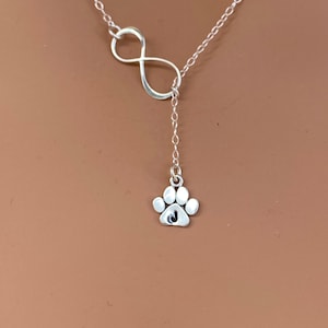 May include: A silver necklace with an infinity symbol charm and a paw print charm with a letter J engraved on it.