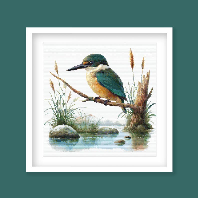 Sacred Kingfisher Kōtare Cross Stitch Pattern displayed as framed wall art with a native New Zealand kingfisher, blue-green feathers, reeds, water, and natural wetland detail.