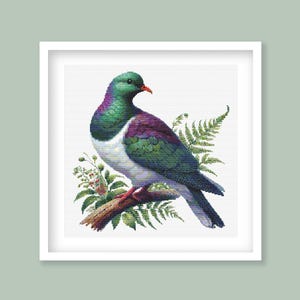 Könnte beinhalten: Eine grüne und violette neuseeländische Taube, auch bekannt als Kereru, sitzt auf einem Ast mit grünen Farnen. Der Vogel hat eine weiße Brust und einen roten Schnabel.