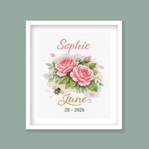 Könnte beinhalten: Gerahmtes Kreuzstich-Kunstwerk mit rosa Rosen, grünen Blättern und einer Biene. Der Name "Sophie" steht über den Rosen, darunter "June 28, 2026". Das Kunstwerk ist in einem weißen Rahmen auf hellgrünem Hintergrund.