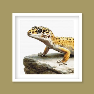 May include: A detailed image of a leopard gecko, featuring a yellow and brown spotted pattern. The reptile is perched on a gray rock, with its head turned slightly to the left. The background is white, and the image is framed in a white square.