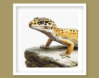May include: A detailed image of a leopard gecko, featuring a yellow and brown spotted pattern. The reptile is perched on a gray rock, with its head turned slightly to the left. The background is white, and the image is framed in a white square.
