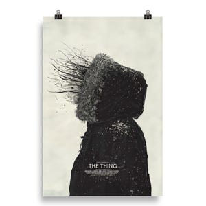 May include: Poster featuring a person in a black parka with a fur-lined hood. The poster has a monochrome color scheme with the title "THE THING" at the bottom. The image has a surreal, artistic quality with abstract elements.