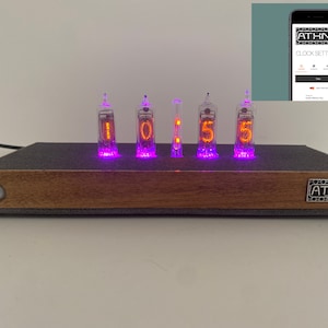 May include: A digital clock with orange glowing numbers, displaying "10:55". The clock has a wooden base and a dark gray top. The clock's brand name, "ATHNK", is displayed on the front. A smartphone screen shows the clock settings.