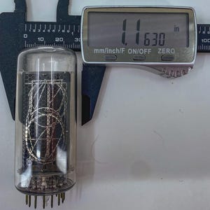 Könnte beinhalten: Eine transparente Vakuumröhre aus Glas mit internen Drahtkomponenten, gemessen mit einem digitalen Messschieber mit 2,95 cm. Die Röhre hat mehrere Stifte an der Basis und ein metallisches Maschendesign im Inneren.