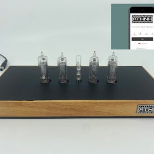 May include: A digital clock with five vacuum tubes on a black surface, set in a wooden frame. The clock has the ATHNH logo and is connected to a power source. A smartphone displays clock settings.