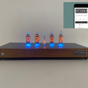 May include: A wooden clock with a black face and five orange Nixie tubes displaying the time "0201". The clock has a silver label with the text "ATHNK" on the front.