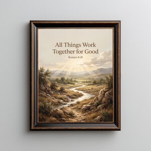 Op de afbeelding: Een ingelijste kunstdruk met een landschapsschilderij van een kronkelende rivier door een vallei met zonnestralen die door de wolken breken. De tekst All Things Work Together for Good Romans 8:28 staat in donkerbruine letters bovenaan in het midden.