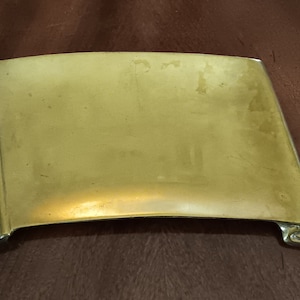 May include: A gold-colored metal scroll-shaped tray with rolled edges. The tray is slightly curved and has a smooth surface.