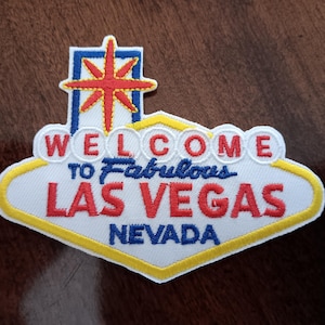 May include: White felt patch with a red, yellow, and blue embroidered design of the iconic Las Vegas sign. The sign reads "Welcome to Fabulous Las Vegas, Nevada".