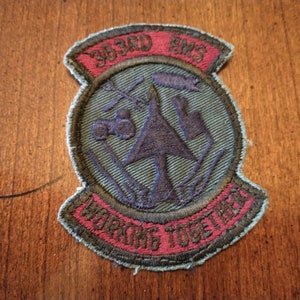 May include: A green, blue, and red embroidered patch with the text "363rd EMS" and "WORKING TOGETHER" in a circle. The patch features a stylized pine tree with a plane flying over it.
