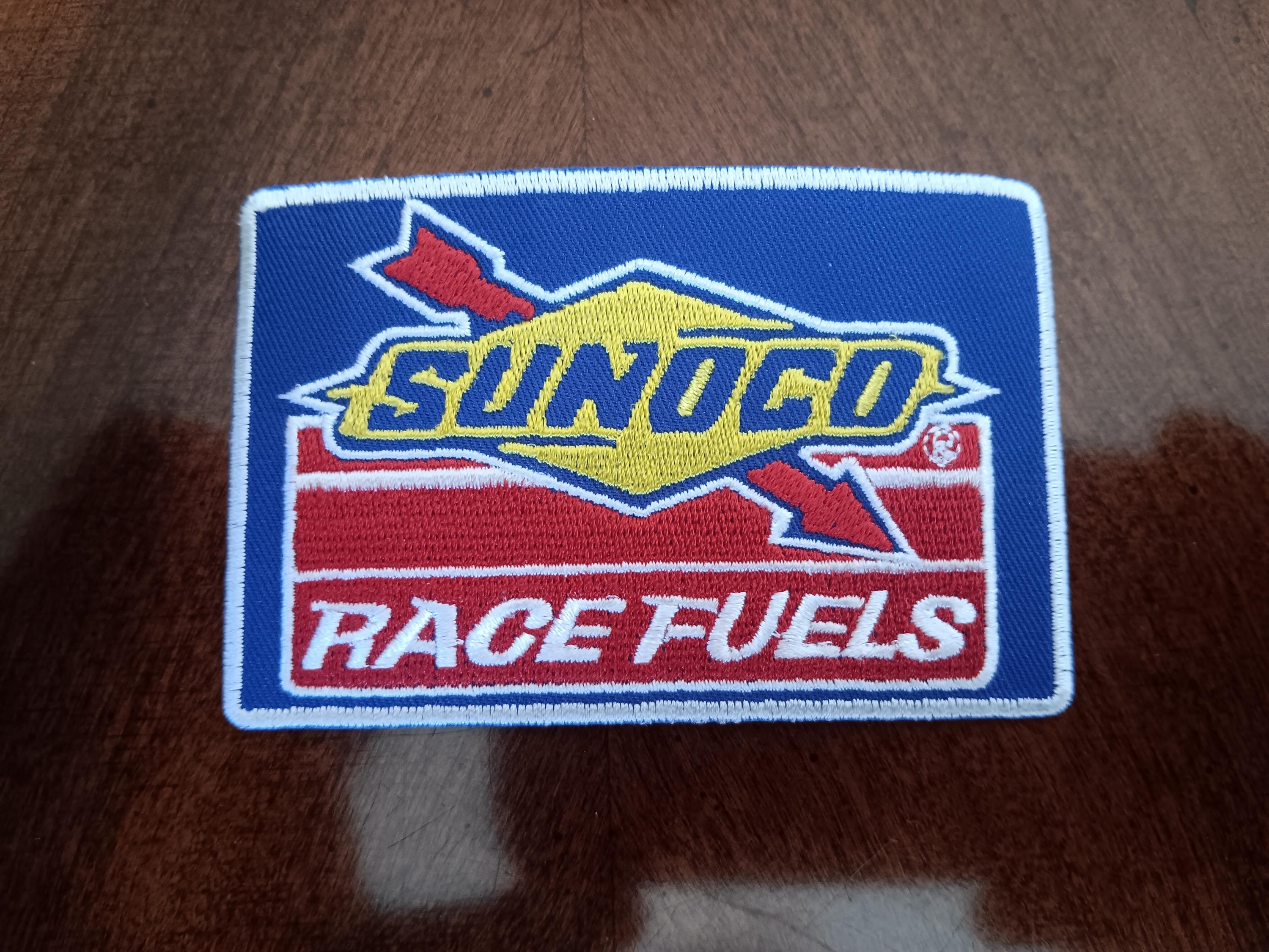 May include: A rectangular embroidered patch featuring the Sunoco Race Fuels logo. The design includes a blue background, a yellow diamond shape with a red arrow, and the text SUNOCO in blue and RACE FUELS in white on a red striped base.