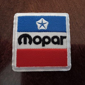 May include: A rectangular embroidered patch featuring a horizontal tricolor design of blue, white, and red. The blue section contains a white pentastar logo. The white center section features the black text MOPAR in a lowercase font.