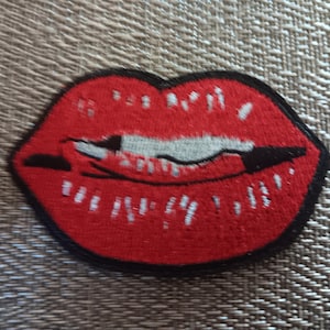 May include: Red embroidered lips with a white and black embroidered detail inside the lips.