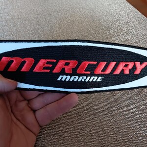 May include: A white, black, and red embroidered patch with the text "MERCURY MARINE" in a white oval on a black background.