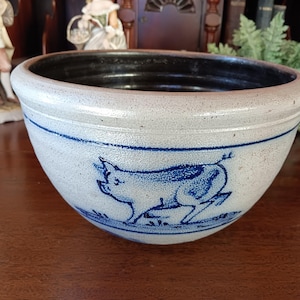 May include: A white ceramic bowl with a blue and white pig design. The bowl has a glazed finish and a slightly rounded shape.