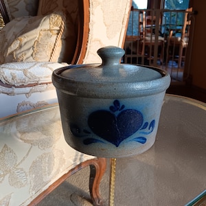 May include: A blue and white ceramic crock with a heart design. The crock has a lid and is sitting on a glass table.