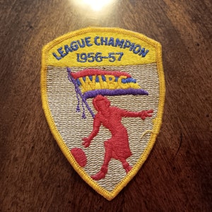 May include: A yellow, white, and red embroidered patch with the text "League Champion 1956-57" and a woman bowling with a flag that says "WIBC".