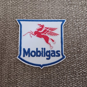 May include: Embroidered patch featuring the Mobilgas logo. The patch has a white background with a red Pegasus in the center. The text "Mobilgas" is in blue. The patch is bordered in blue.