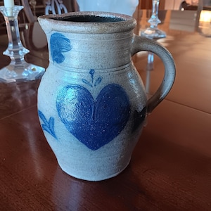 May include: A blue and white ceramic pitcher with a heart design. The pitcher has a handle and a spout.