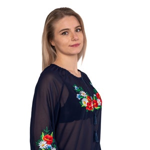 May include: Navy blue blouse with long sleeves and floral embroidery. The embroidery features red poppies, white daisies, and green leaves. The blouse has a round neckline and tassel details.